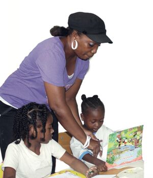 Maestra trabaja con dos niñas con libro de lectura.