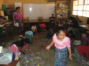 Salón de clases con maestra y estudiantes indígenas.png